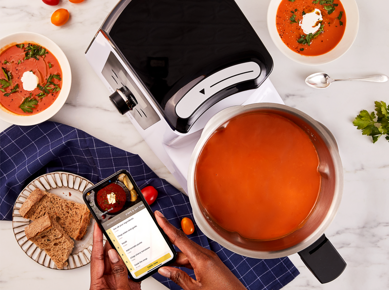 Overhead image of a phone with the Gourmate appliance. Mixing bowl contains tomato soup. Phone contains the recipe for the soup.